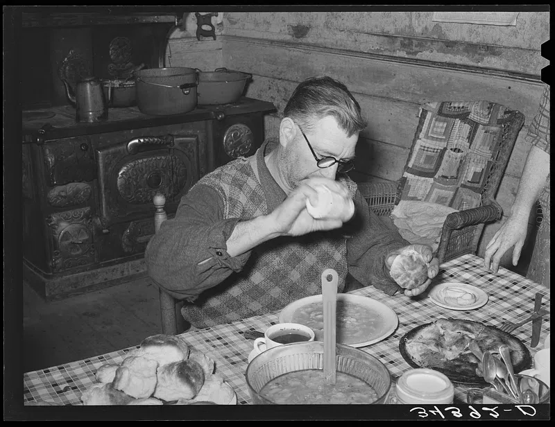 a photo that looks old in which a man is eating what I assume are soup beans.